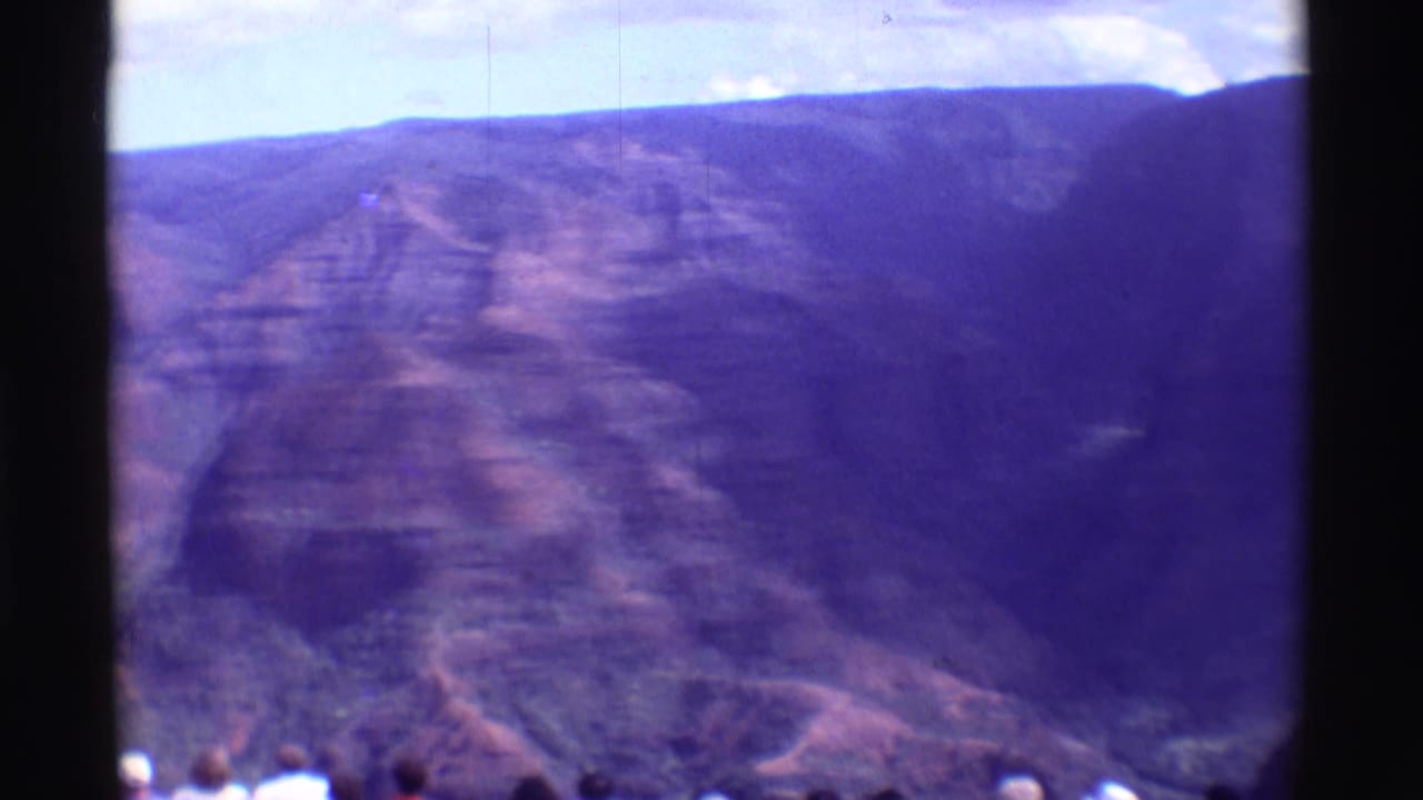 Canyon overlook view with layered cliffs, dark film divider, and small tourists along the bottom edge.