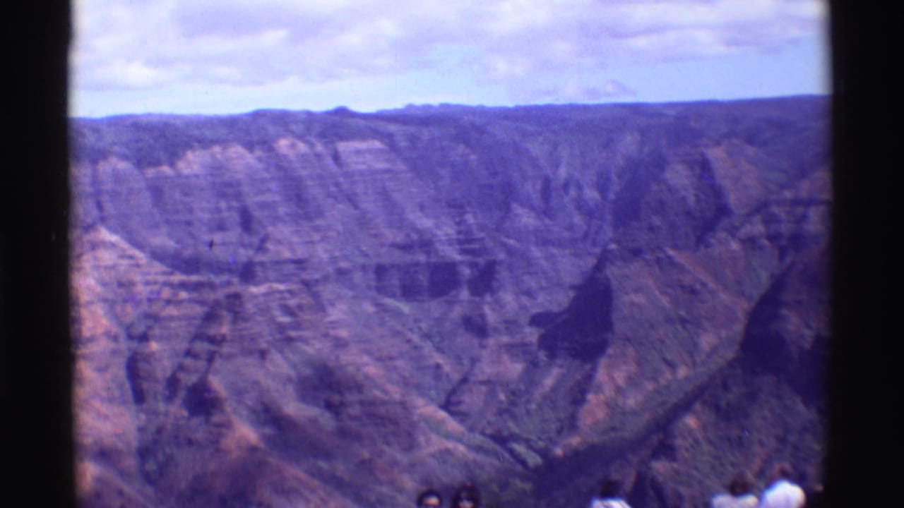 1971 Mauna Ulu frame with layered volcanic canyon walls, distant visitors at the overlook, dark scan borders, and a pale clouded sky.