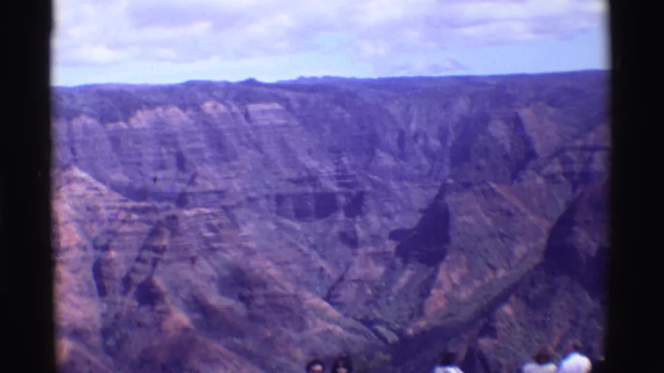 1971 Mauna Ulu frame with layered volcanic canyon walls, distant visitors at the overlook, dark scan borders, and a pale clouded sky.