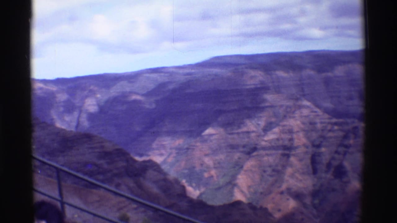 1971 8mm travel view from an overlook, with railing and partial visitors at the bottom edge before steep canyon walls.