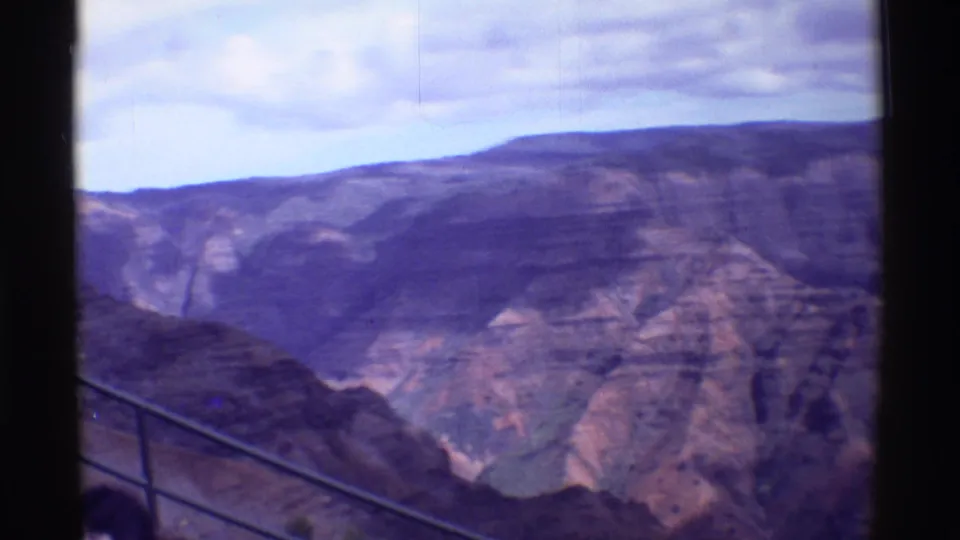 1971 8mm travel view from an overlook, with railing and partial visitors at the bottom edge before steep canyon walls.