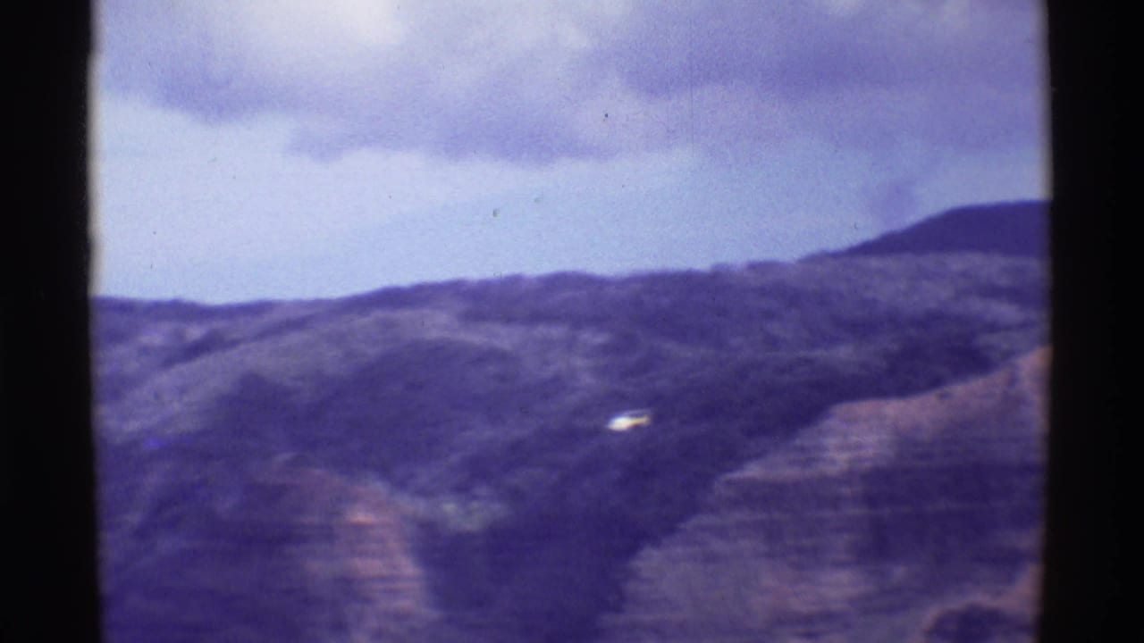 Distant helicopter over a hazy canyon and hills beneath clouds.