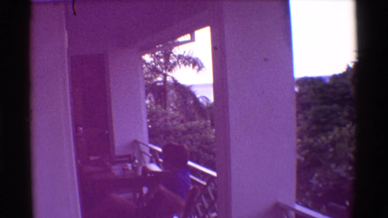 Balcony scene with a seated child, small table, white columns, railing, trees, and distant water.