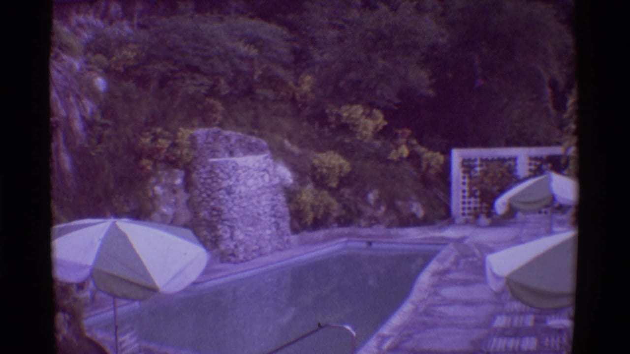 1971 Mauna Ulu, Hawaii frame with a quiet pool terrace, white umbrellas, stonework, deck paving, and dense hillside vegetation.