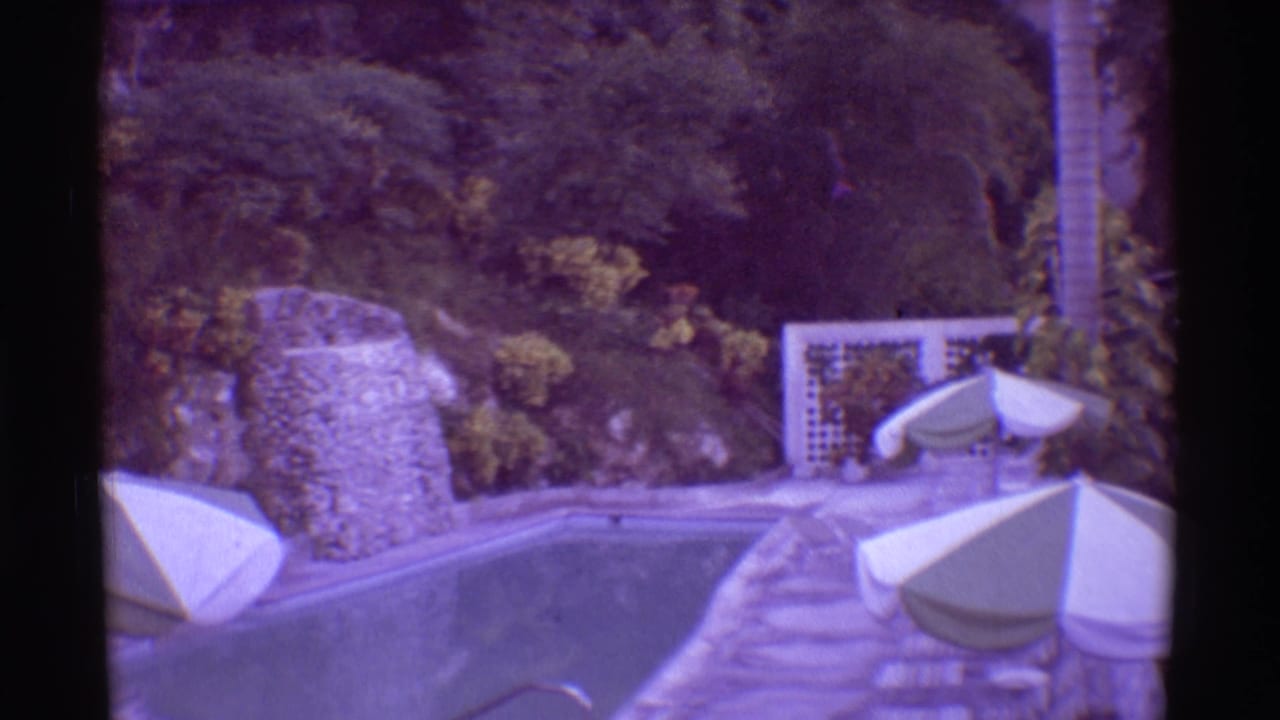 1971 Mauna Ulu, Hawaii frame of a poolside terrace with white umbrellas, lounge furniture, stone walls, and surrounding tropical growth.