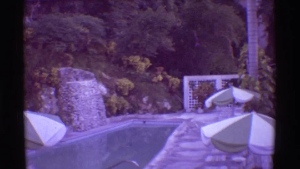 1971 Mauna Ulu, Hawaii frame of a poolside terrace with white umbrellas, lounge furniture, stone walls, and surrounding tropical growth.