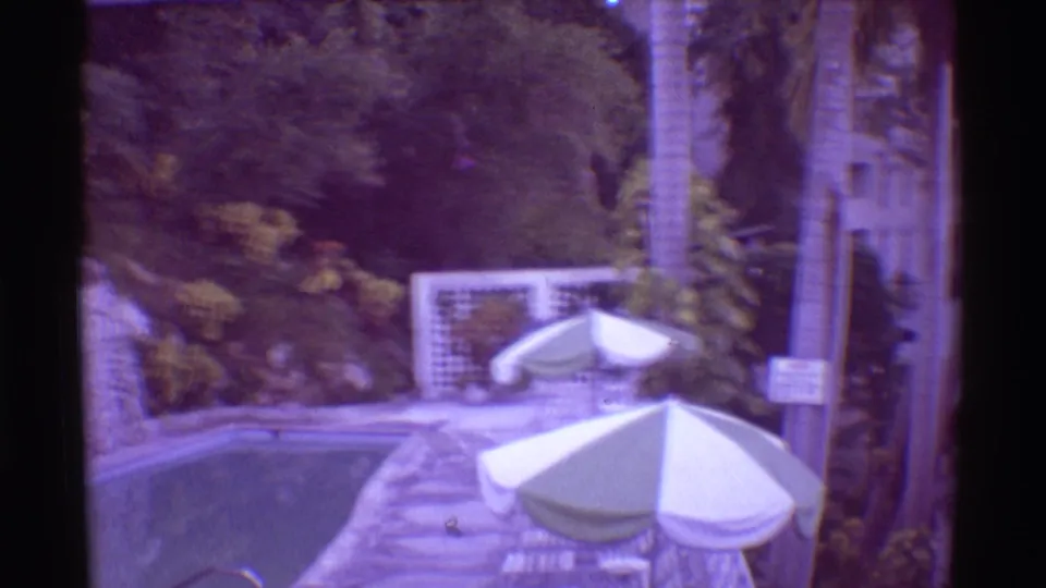1971 Hawaii resort pool area with umbrellas, palms, tropical plants, and a sign beside the path.