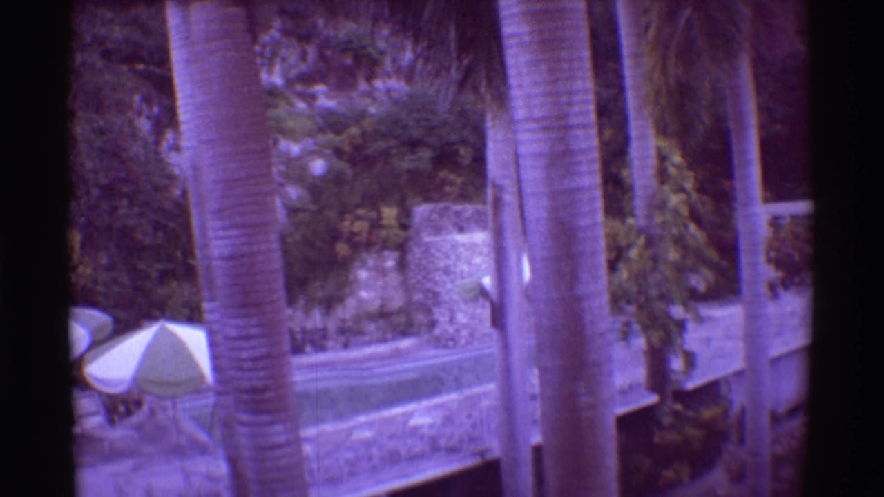 1971 Hawaii 8mm frame showing palms and resort buildings with a small pool umbrella and landscaped courtyard below.