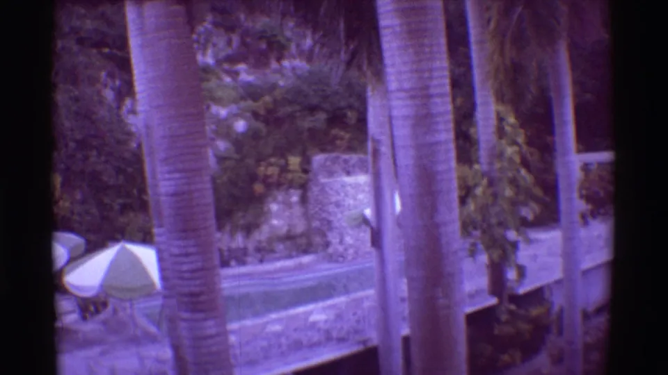 1971 Hawaii 8mm frame showing palms and resort buildings with a small pool umbrella and landscaped courtyard below.