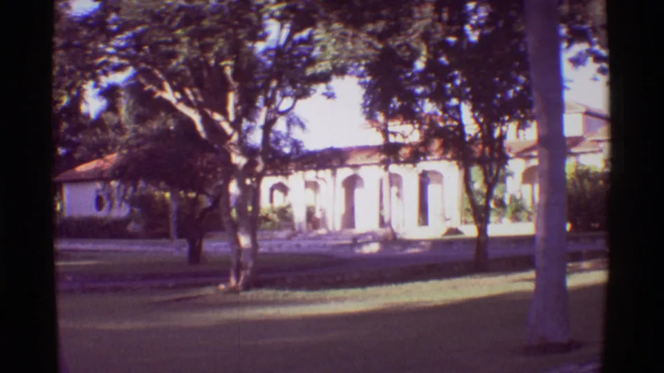 1971 Hawaii home-movie frame showing a white arched building partly screened by trees and a sunlit lawn.