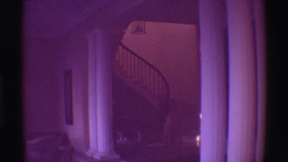 1971 Hawaii estate interior with white columns, a shadowed hallway, and a curved staircase under a purple film cast.