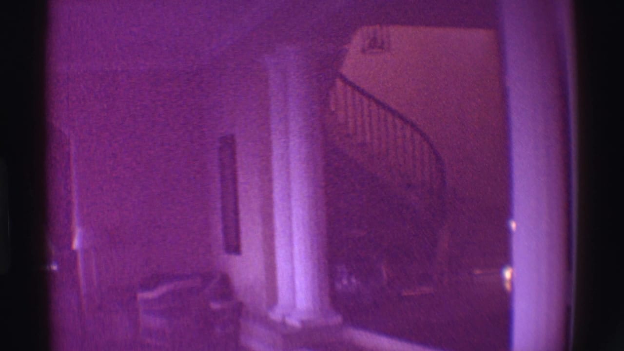 Purple-tinted 1971 Hawaii home-movie frame of an estate interior with columns, seating, and a spiral staircase area.