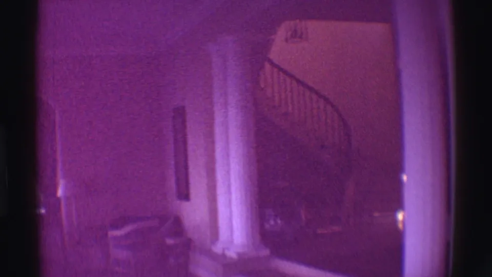 Purple-tinted 1971 Hawaii home-movie frame of an estate interior with columns, seating, and a spiral staircase area.