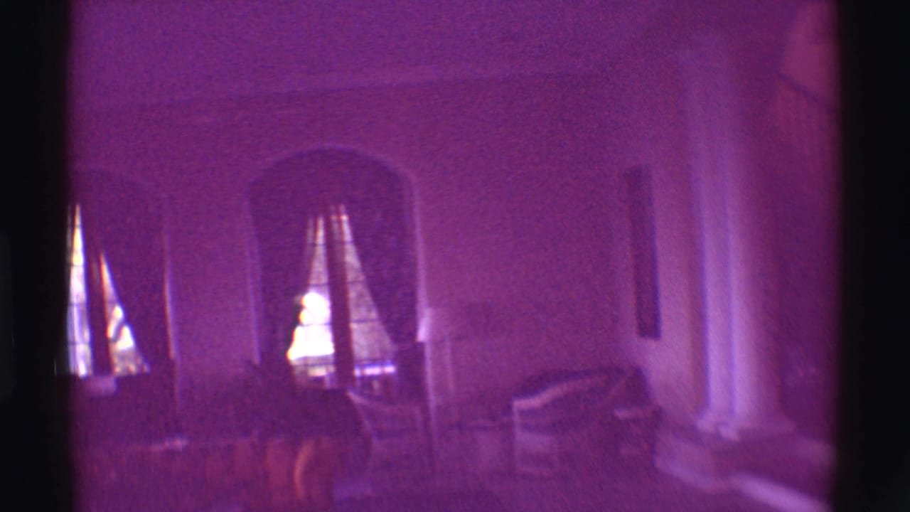 1971 Hawaii interior frame showing a living room with arched windows, curtains, chairs, columns, and a pronounced purple color cast.