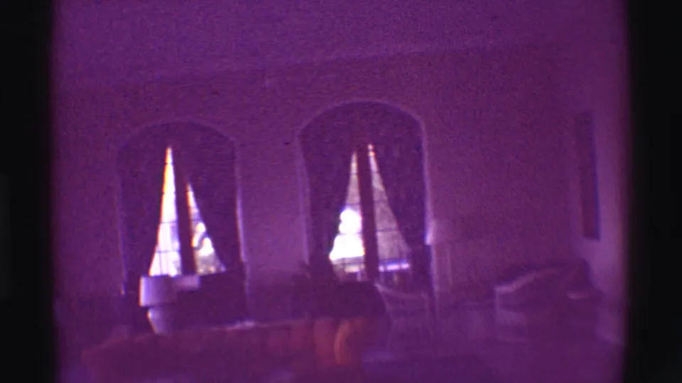 1971 Hawaii 8mm frame of a dim private interior with arched openings, curtains, furniture and strong purple color shift.