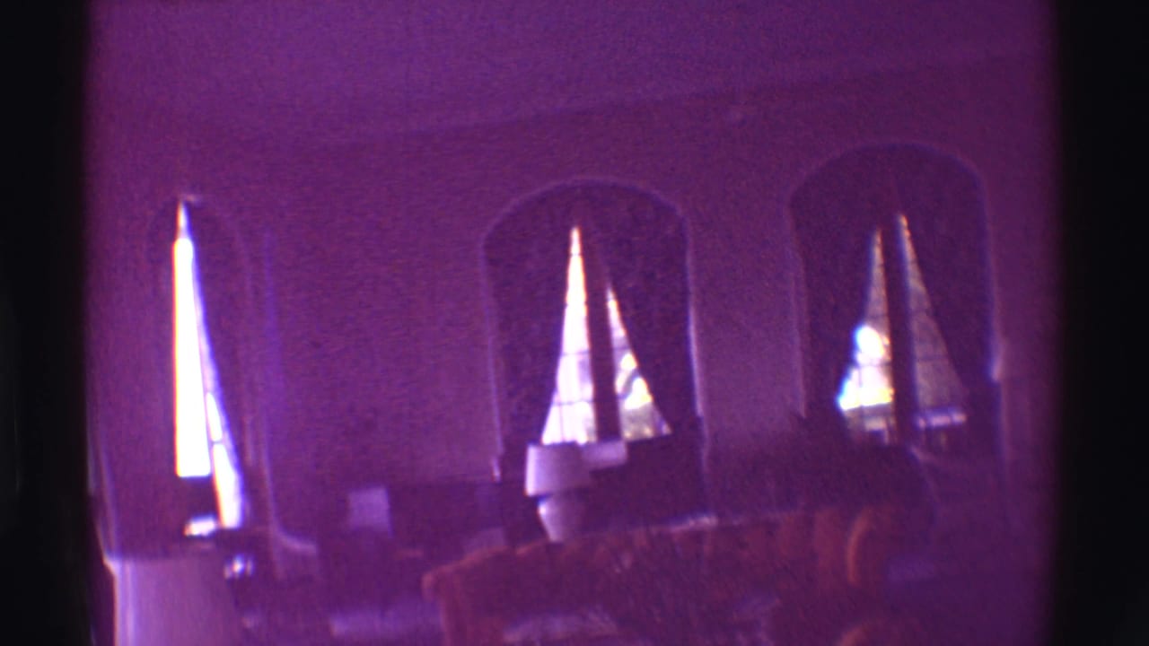 Dim room with arched window openings, curtains and a chair silhouetted at right.