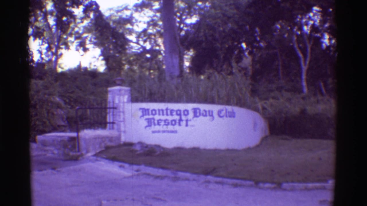 1971 8mm Hawaii travel frame centered on the Montego Bay Club Resort sign near a gated entrance, trees, grass, and roadside pavement.