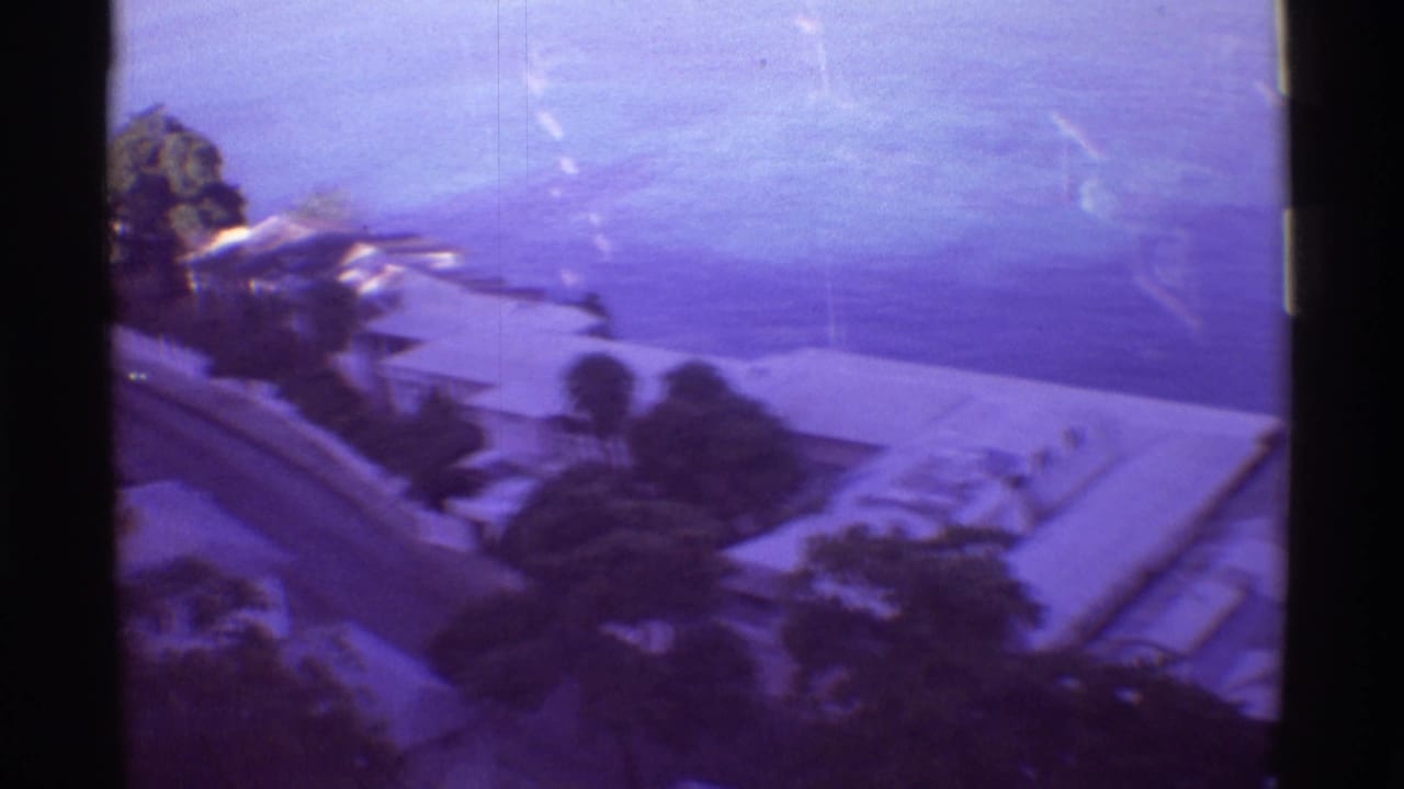 1971 Hawaii home-movie frame showing a blurred hillside view of coastal residences and ocean beyond.