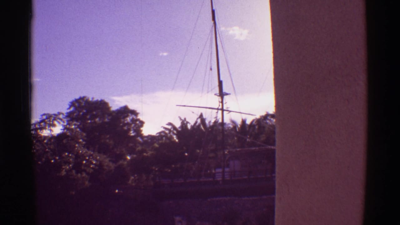 1971 Hawaii 8mm frame showing a sailboat mast and rigging near a harbor, with dense foliage and a building column in the foreground.