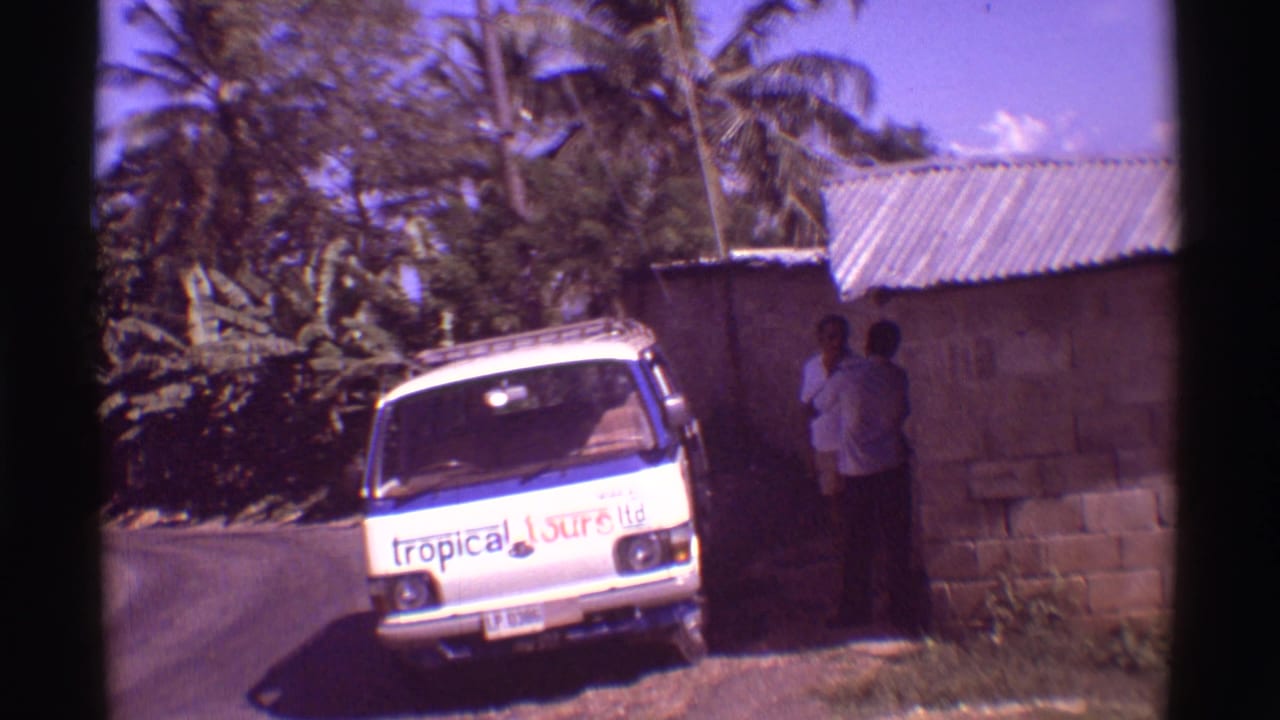 1971 Hawaii 8mm frame showing a white branded tour van near a cinder block building under palm trees.