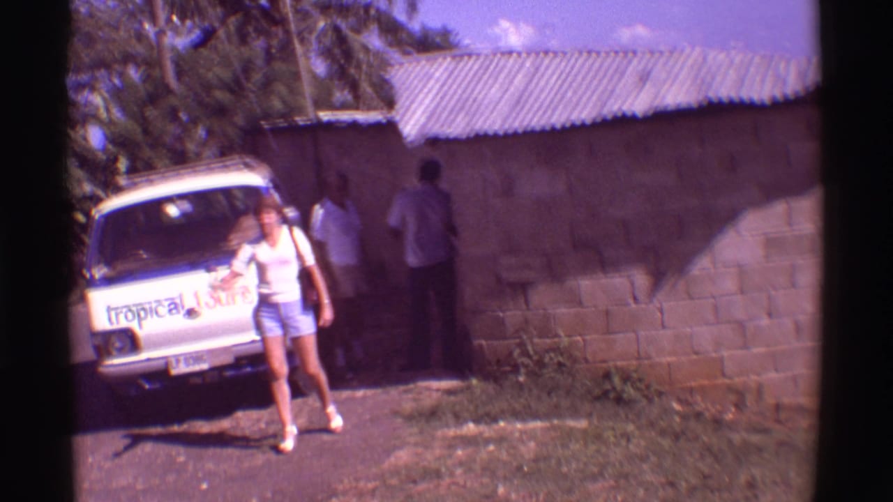 Woman walking from a white tour van while two men stand near a small building.