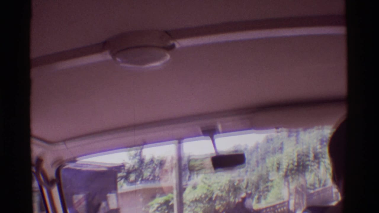 Car interior seen from the passenger area with windshield, rearview mirror, and a dark foreground passenger silhouette.