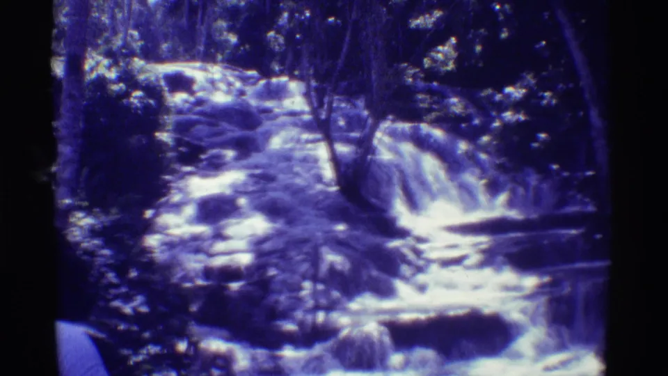 1971 Mauna Ulu, Hawaii home-movie frame of a low jungle waterfall flowing across rocks in blue-purple 8mm color.