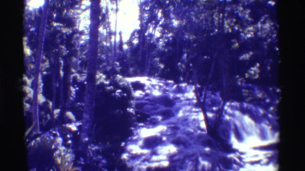 1971 Hawaii home-movie frame of a rocky waterfall, with a partial person or shoulder visible at the lower left edge.