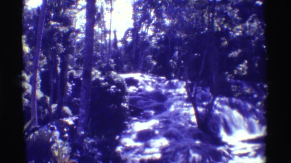 1971 Hawaii home-movie frame of a rocky waterfall, with a partial person or shoulder visible at the lower left edge.