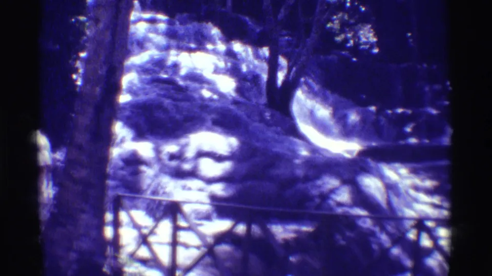 1971 Hawaii 8mm frame shifting away from the people toward the waterfall, railing, rocks, and shaded trees at the overlook.