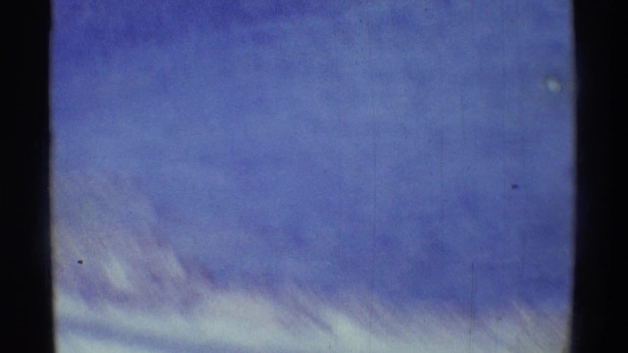 Handheld 8mm frame drifting to a soft blue sky with pale clouds and visible film grain.
