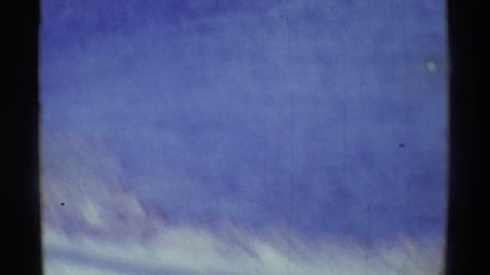 Handheld 8mm frame drifting to a soft blue sky with pale clouds and visible film grain.