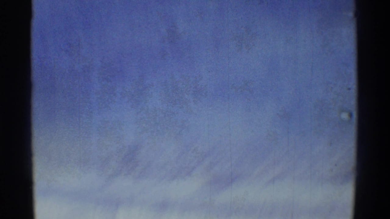 Final handheld frame showing a hazy blue sky with faint cloud streaks and 8mm film texture.