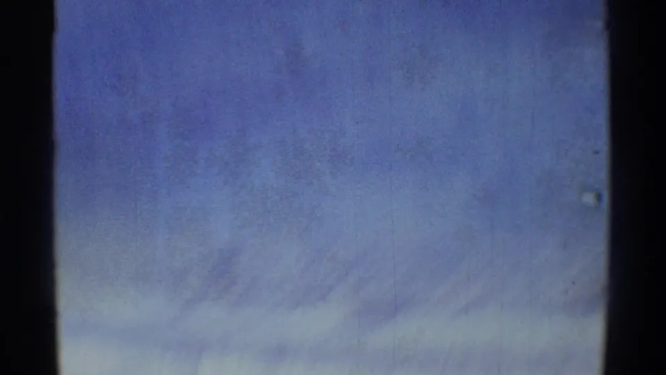 Final handheld frame showing a hazy blue sky with faint cloud streaks and 8mm film texture.