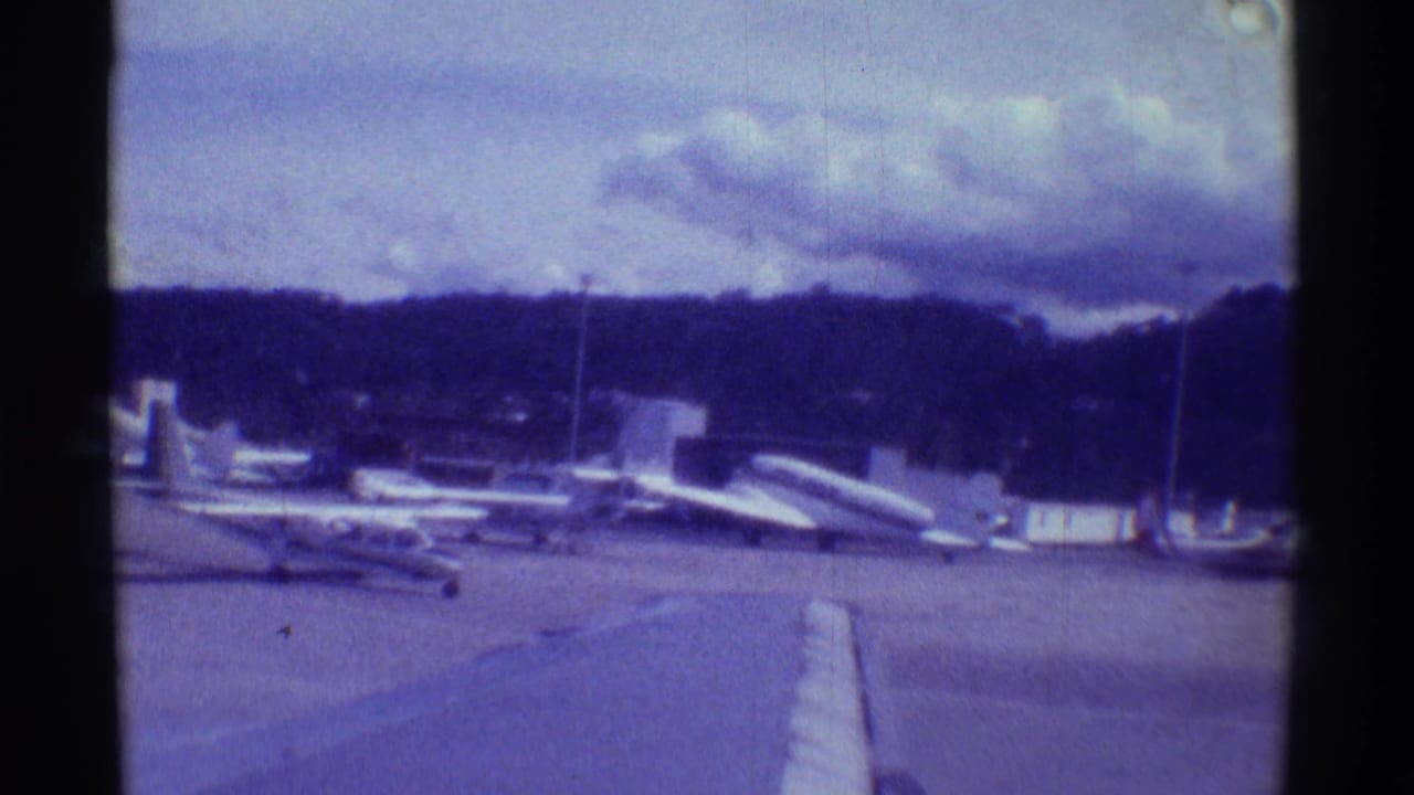 Wide 1971 Hawaii airfield view with multiple parked aircraft, tarmac, low hills, and cloudy sky.