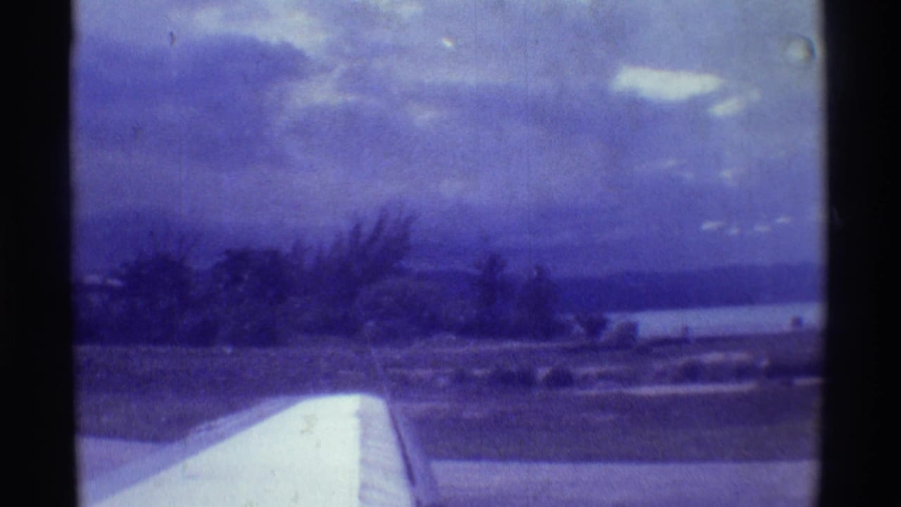 Airplane wing points toward low trees, coastline, water, and a clouded horizon.