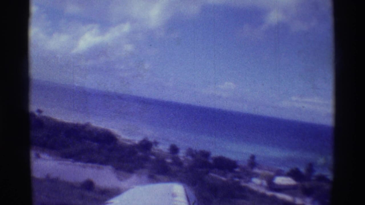 Plane wing over a blue tropical coastline with dark film-frame edges.