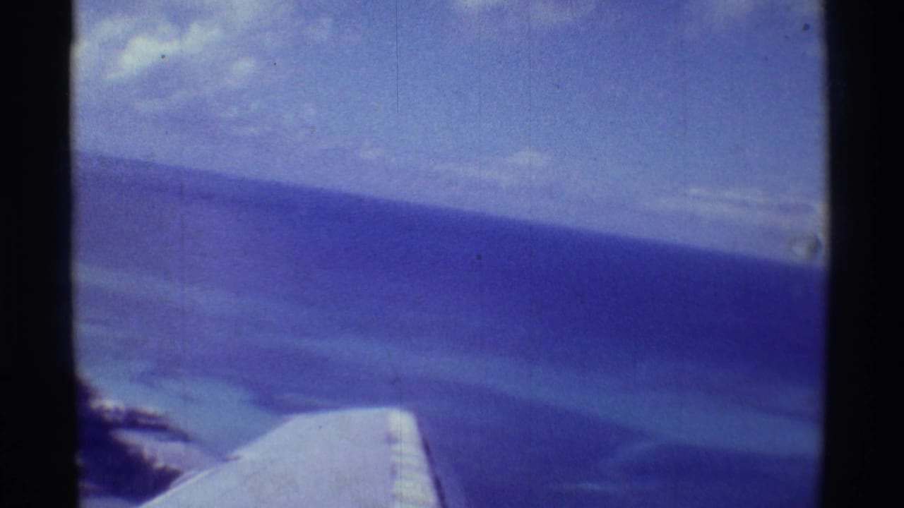 1971 Hawaii passenger-plane view with wing, expansive blue ocean, pale shallows, and distant coast.
