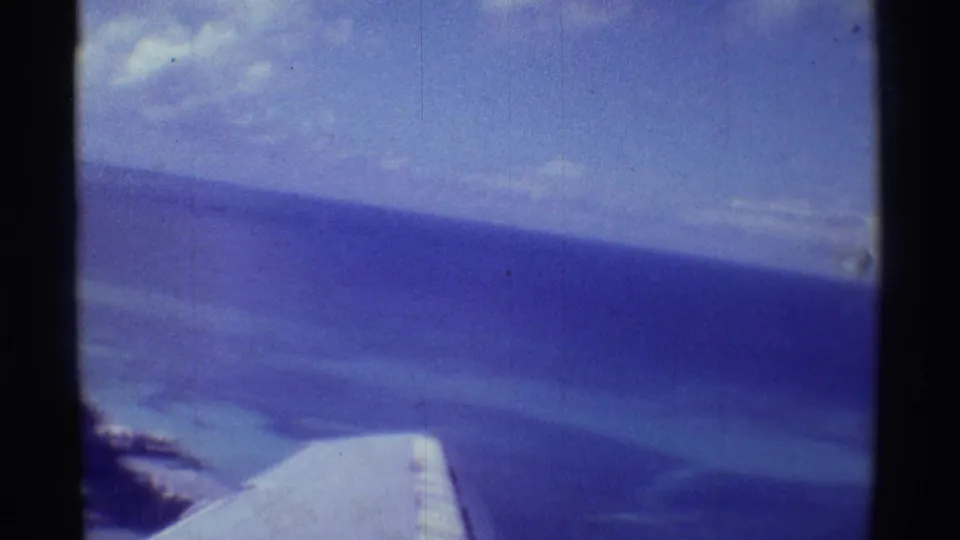 1971 Hawaii passenger-plane view with wing, expansive blue ocean, pale shallows, and distant coast.