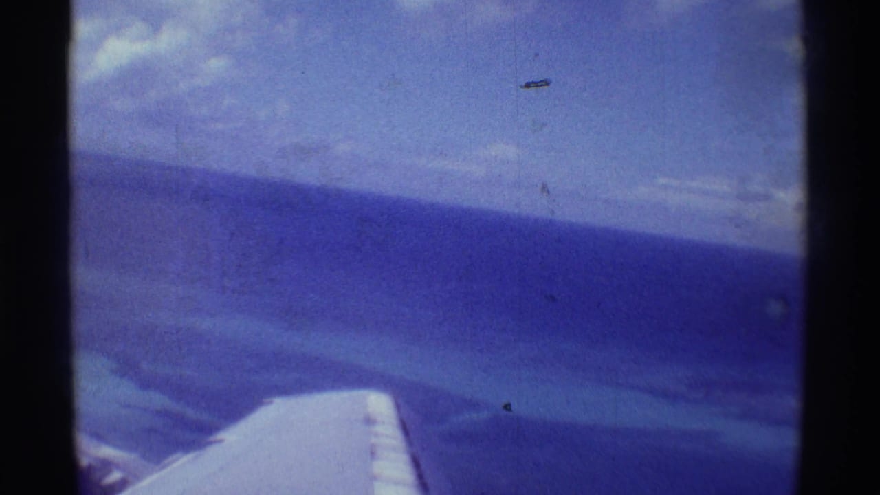 Airplane wing seen through a window above blue ocean and horizon.