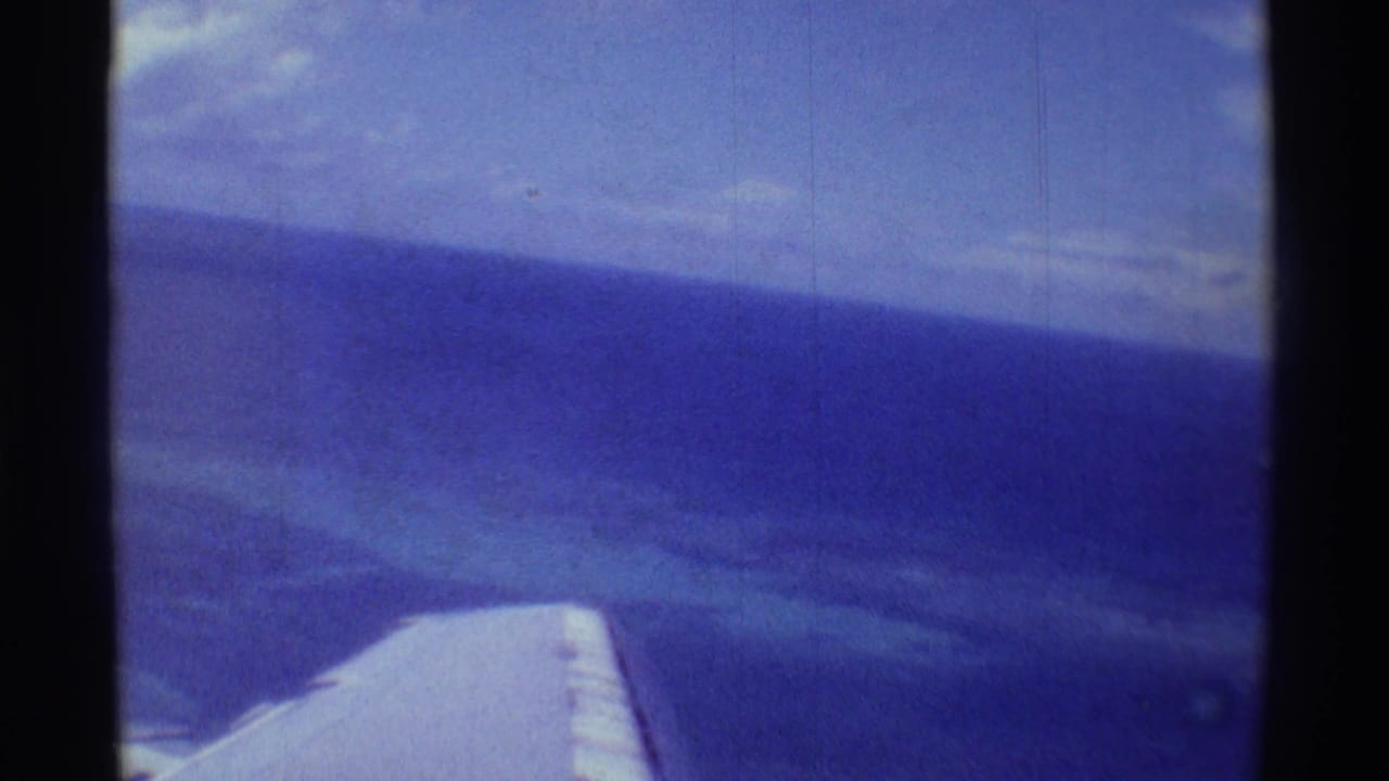 Plane wing at lower frame with blue ocean and sky beyond.
