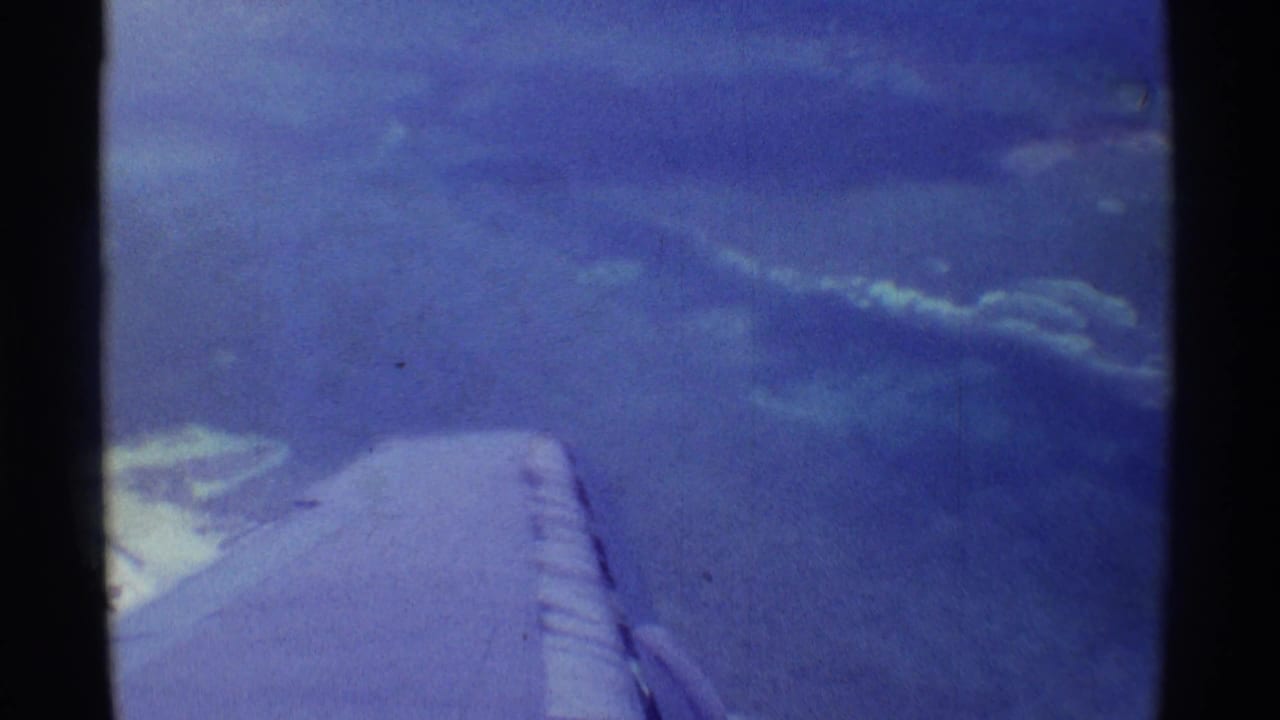 1971 8mm airplane-window view over Hawaii-area ocean, with the wing in the lower frame and clouds spread across the water.