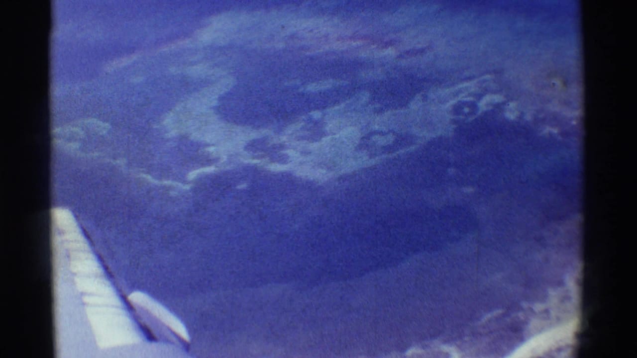 Airplane wing over blue-tinted volcanic terrain and cloud patches.