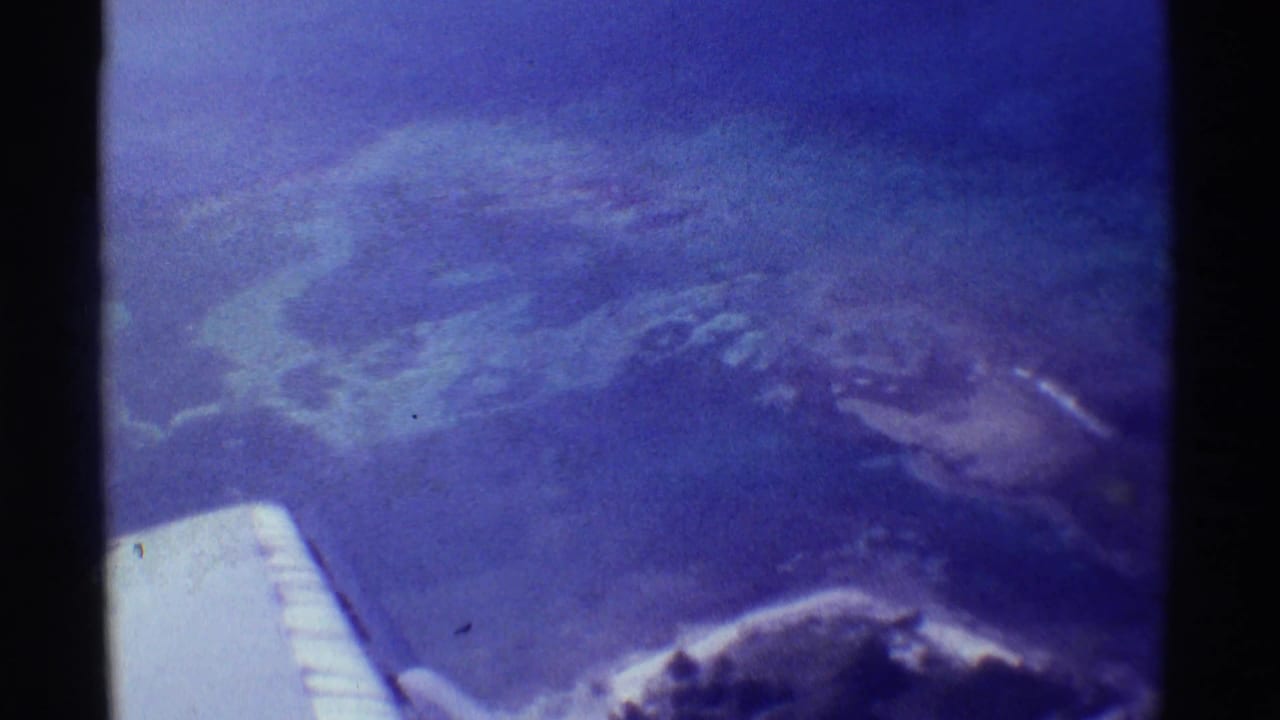 Passenger-shot 1971 aerial frame over Mauna Ulu, showing the wing tip, blue-tinted ground, and scattered white cloud forms.