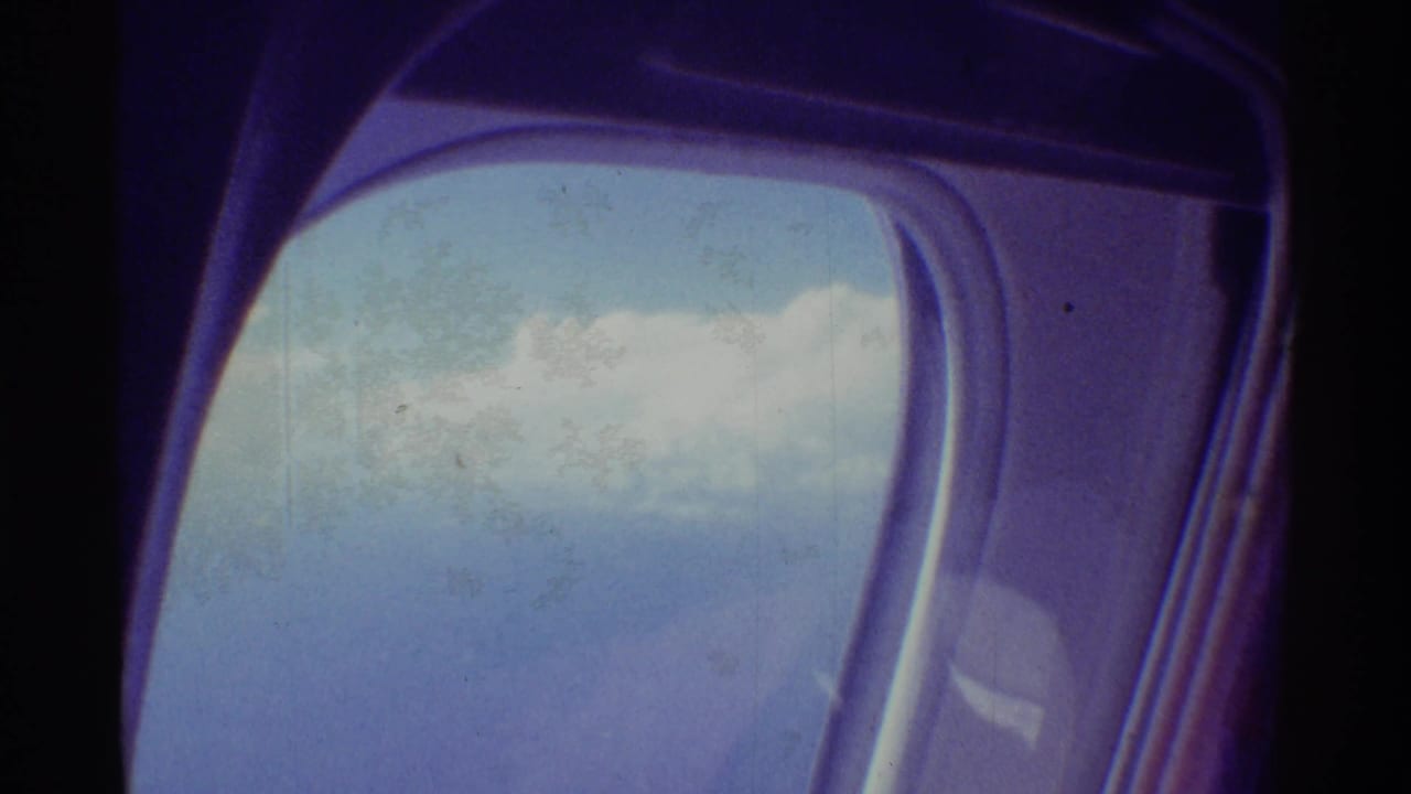Rounded airplane window with blue sky and clouds beyond dark cabin edges.