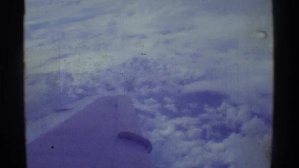1971 8mm Hawaii travel frame showing layered clouds, pale sky, and a partial airplane wing or wingtip from a passenger viewpoint.