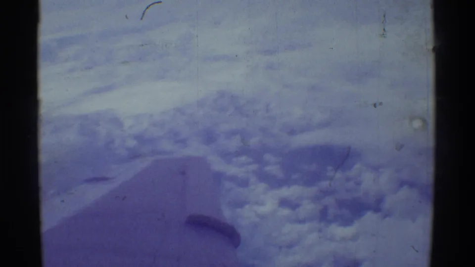 Aerial 8mm frame over Hawaii showing a cloud bank, blue sky, and the airplane wing edge within visible film borders.