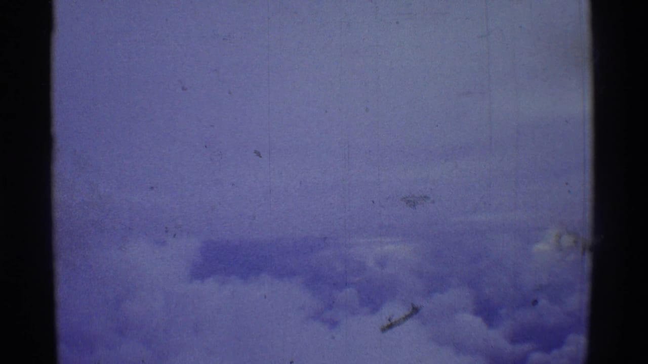 Blue-shifted 1971 8mm aerial frame with faint cloud layers below and heavy film texture across the image.