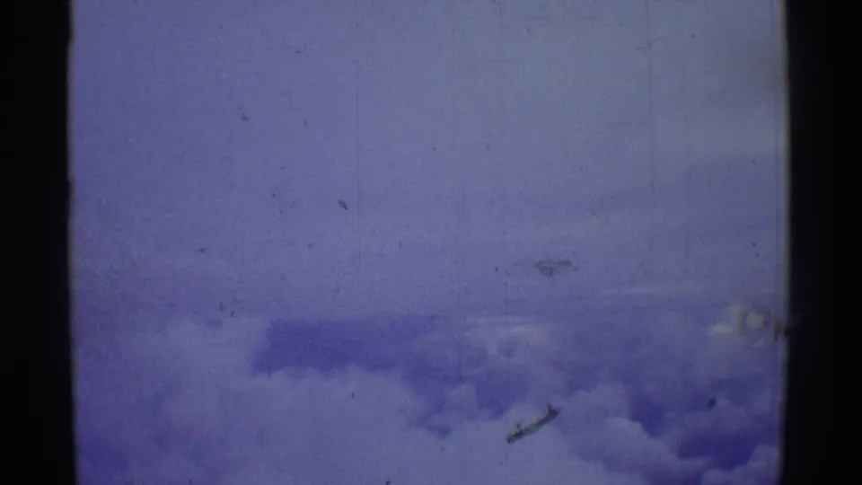 Blue-shifted 1971 8mm aerial frame with faint cloud layers below and heavy film texture across the image.