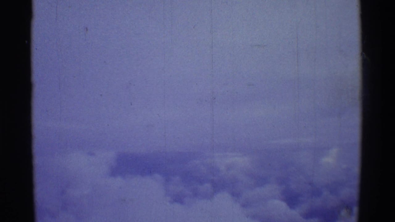 Final 8mm travel frame showing a pale aerial cloud view over Hawaii with scratches, dust, and blue color drift.